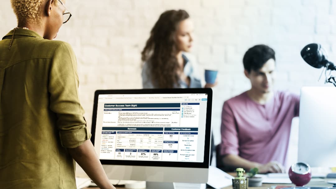 A female office worker reviews her Smartsheet dashboard, co-workers blurred in the background