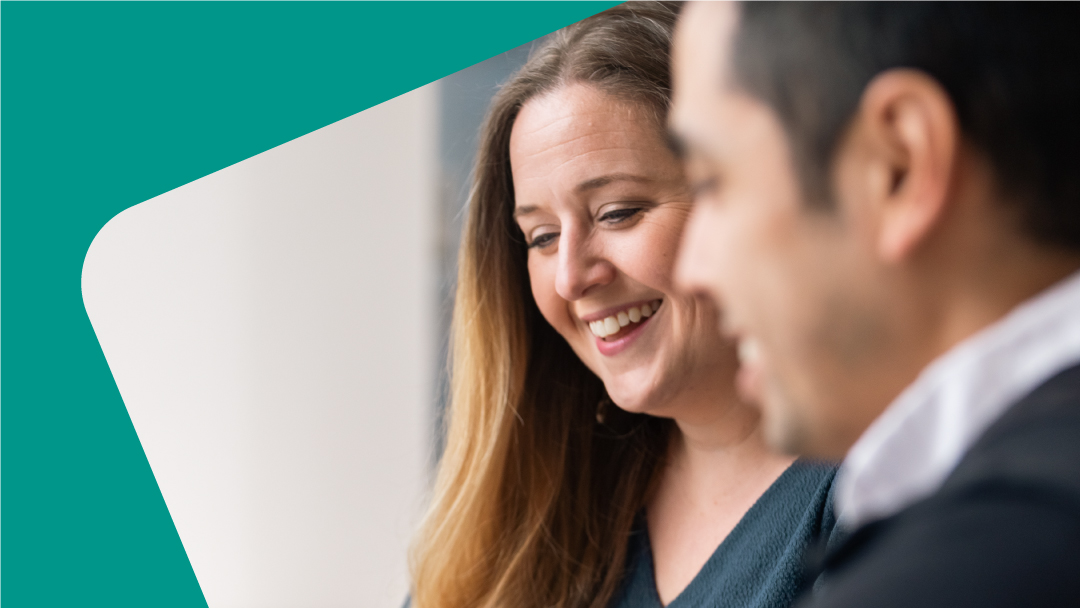 A woman and a man smiling in an office while sitting next to each other